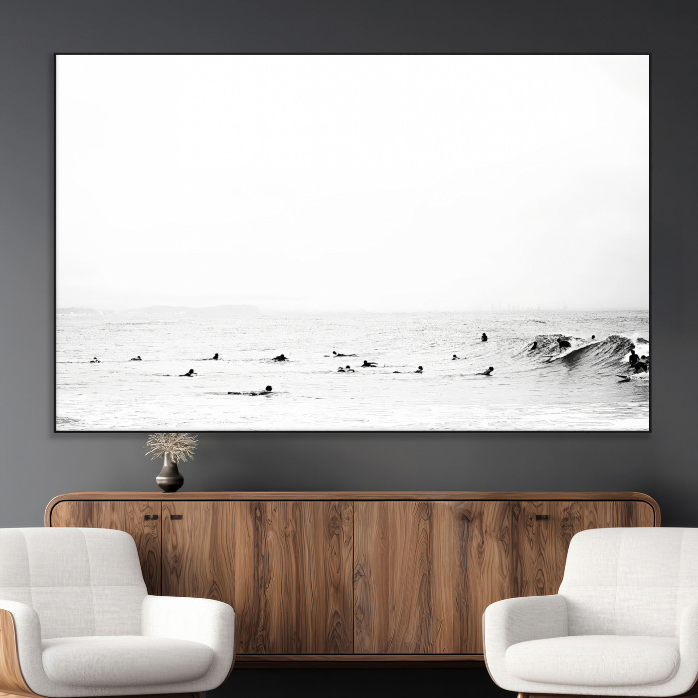 A group of surfers floating in the ocean, waiting for waves under a vast, moody sky, captured in black and white.