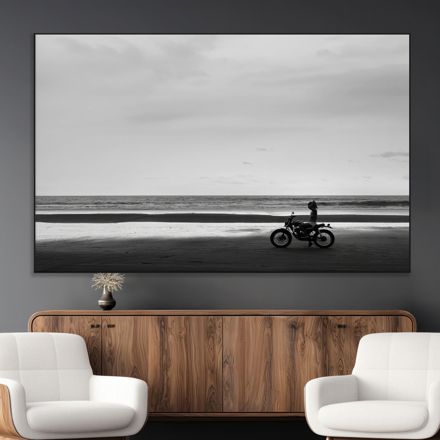 A motorcyclist on a vast beach, gazing at the ocean, capturing a moody and tranquil coastal adventure in black and white.