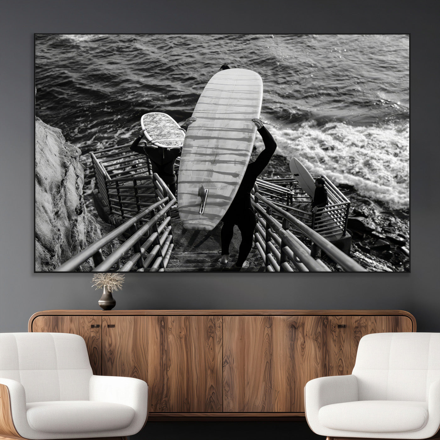 Black and white photo of surfers carrying boards down a rugged cliffside stairway, capturing a bold and adventurous coastal scene.