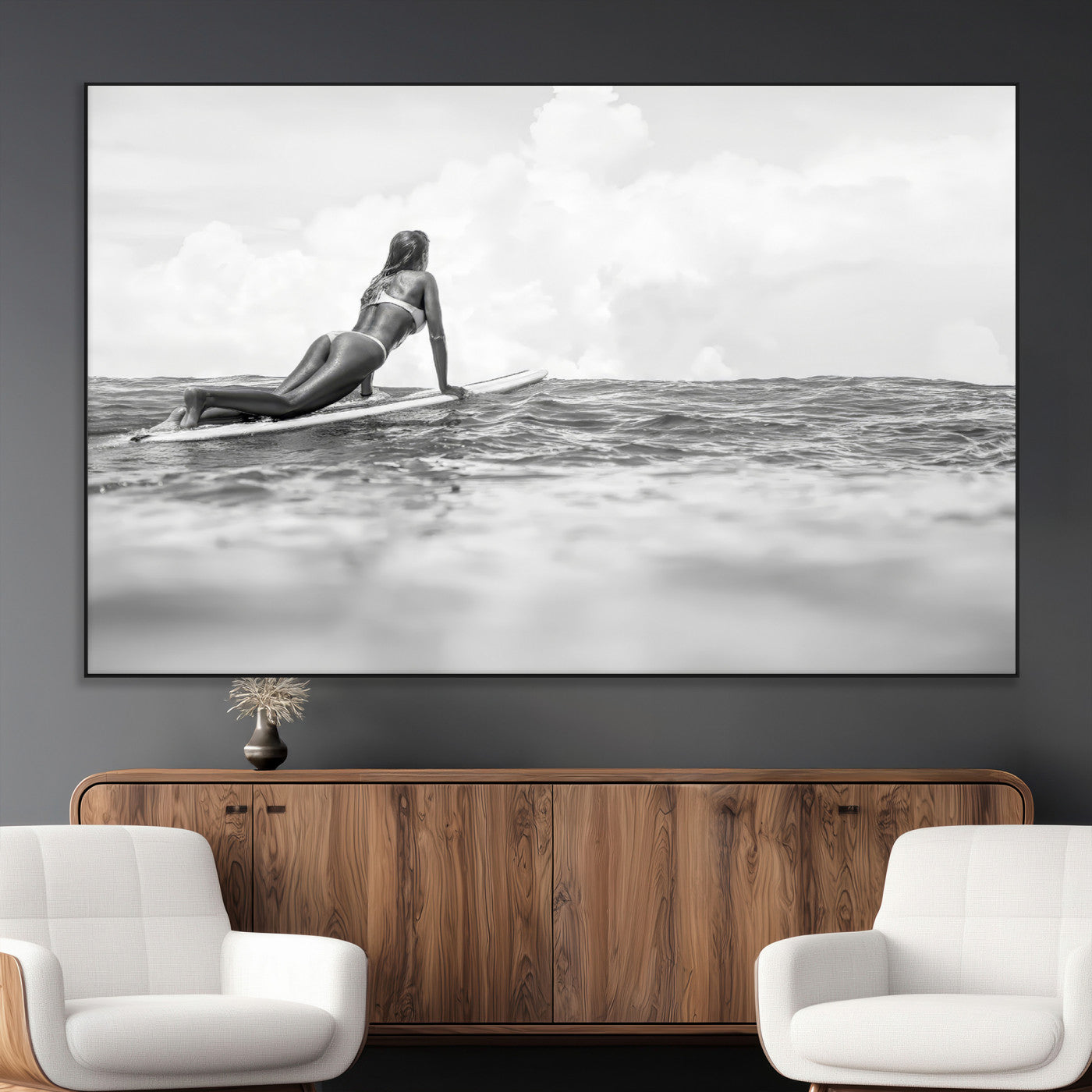 A black and white ocean scene featuring a surfer girl waiting on her board, gazing at the horizon, capturing a tranquil and adventurous coastal moment.
