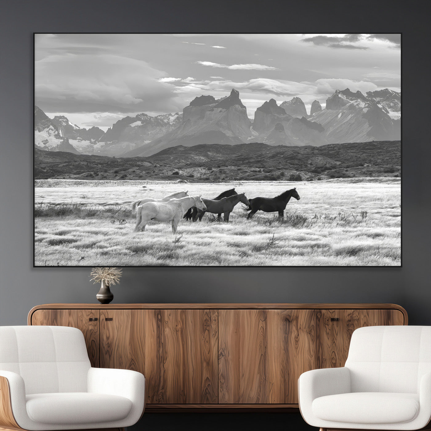 A black and white landscape of wild horses grazing in a vast grassland with towering mountains in the background, creating a moody and rustic western aesthetic.