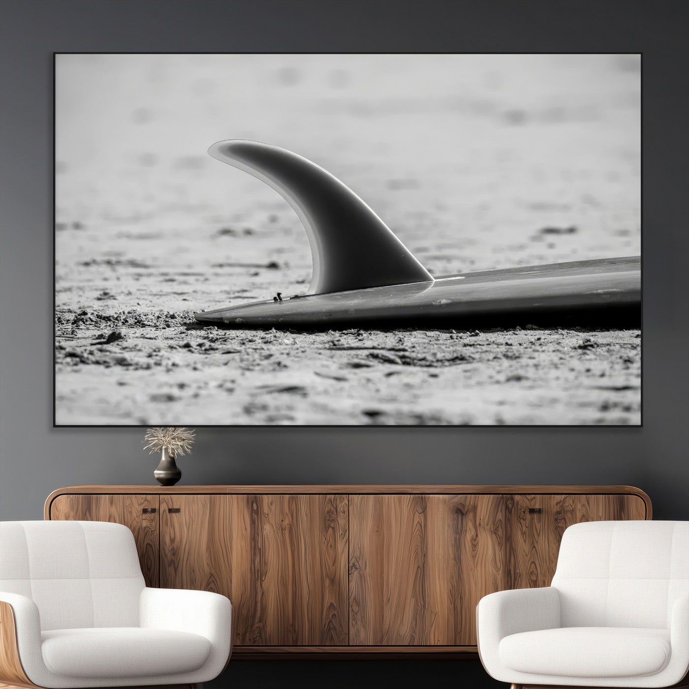 A black and white close-up of a surfboard fin resting on the sandy shore, highlighting minimalist beach aesthetics and classic surf culture.