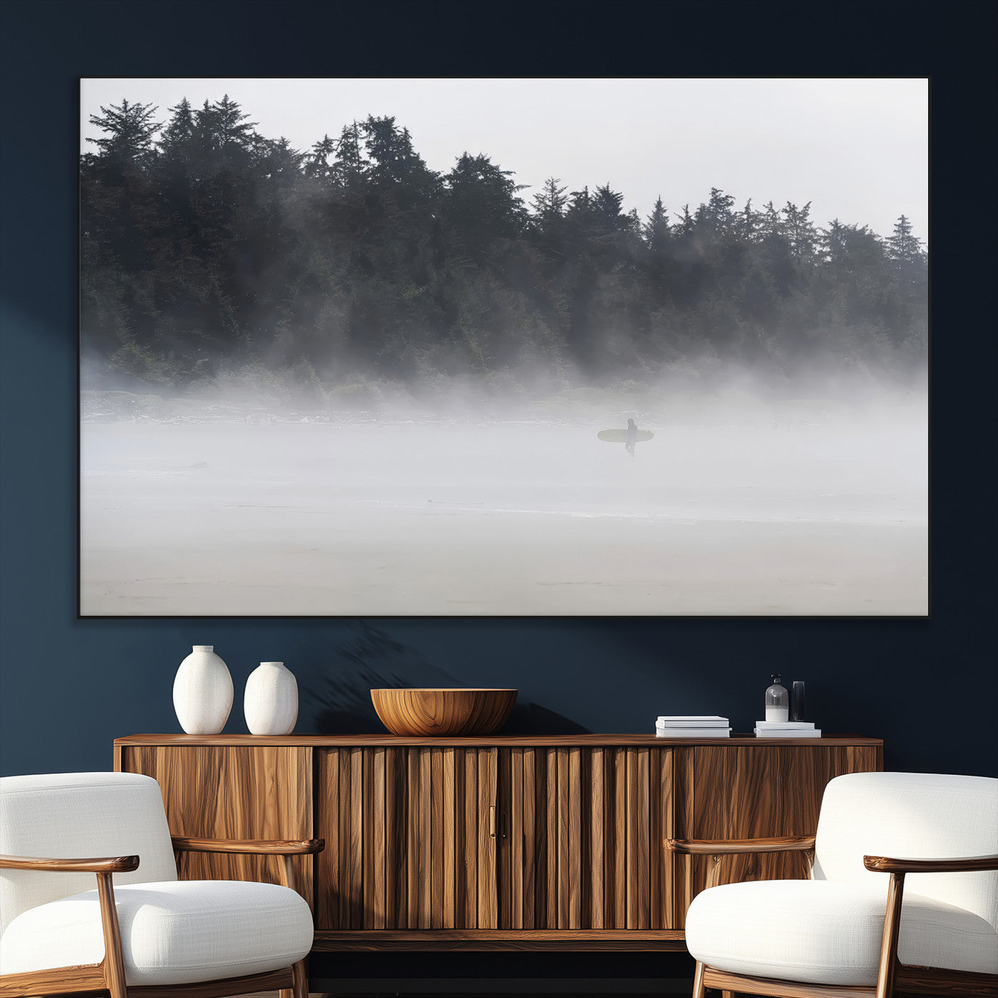 A lone surfer carrying a board through a misty shoreline, surrounded by dense trees and fog, creating a peaceful and mysterious coastal scene.