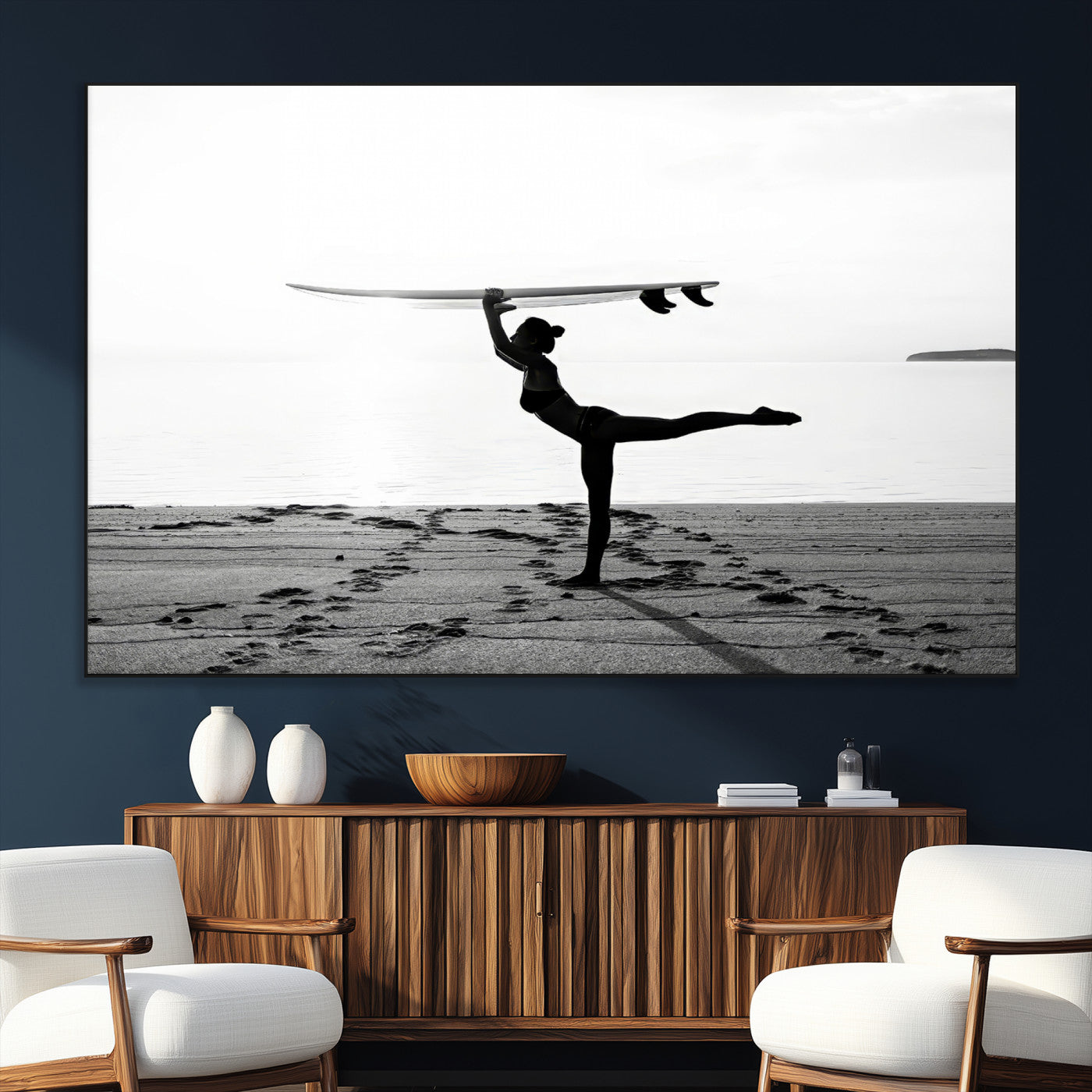 A woman balances a surfboard on her head while striking a yoga pose on the beach, silhouetted against a calm ocean horizon.