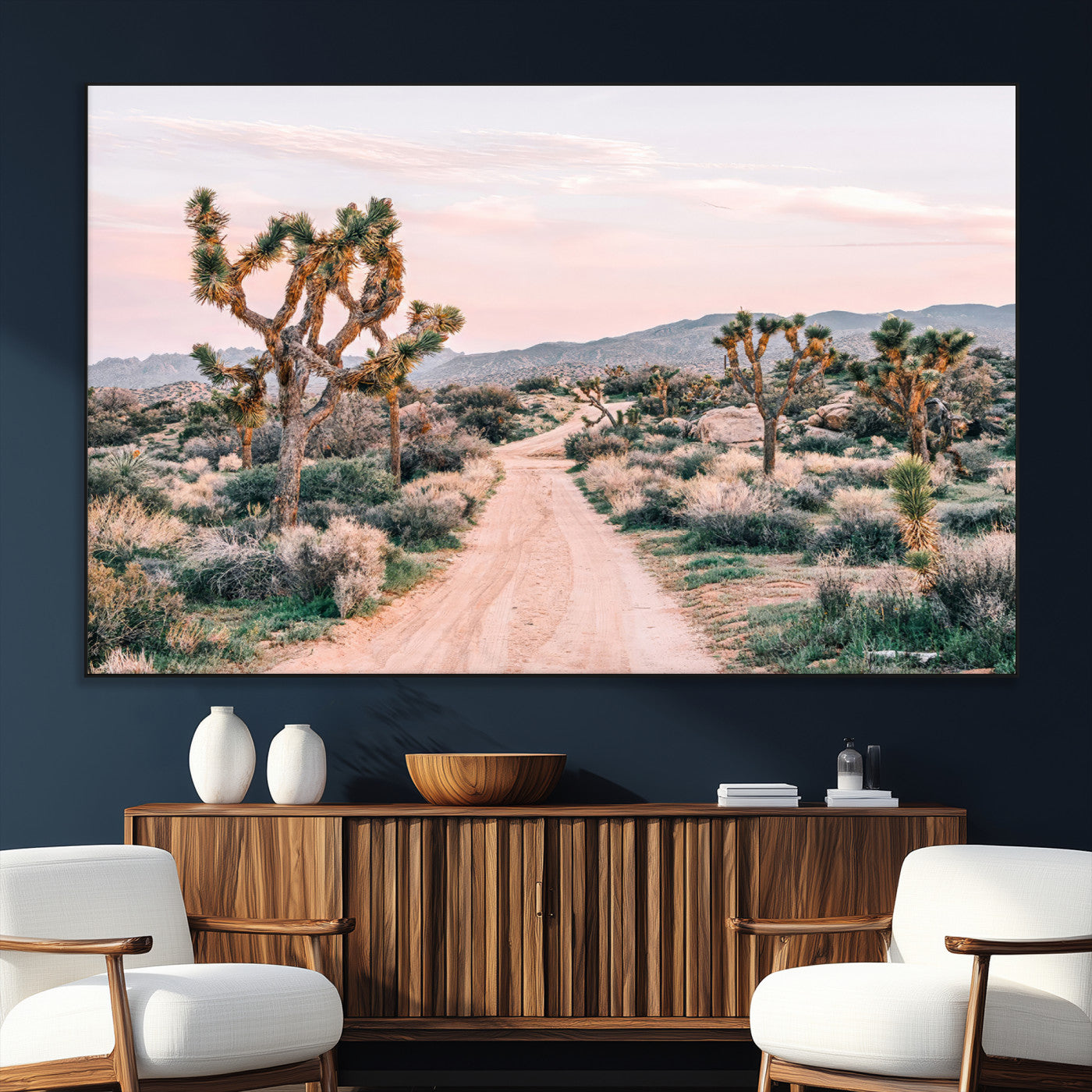 A dusty road winding through Joshua Tree National Park, framed by iconic twisted trees and warm desert tones under a soft pastel sky.