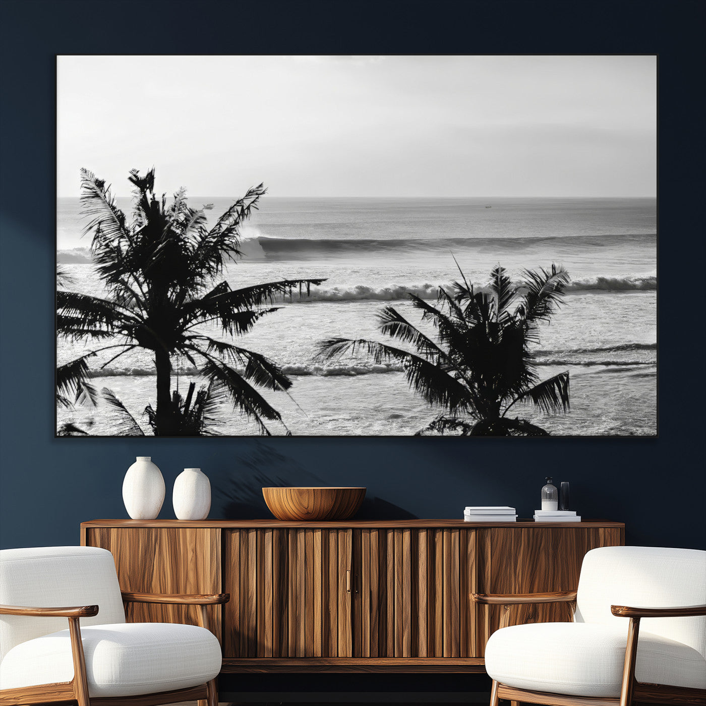 Black and white view of ocean waves crashing on a tropical coastline, framed by silhouetted palm trees under a vast, open sky.