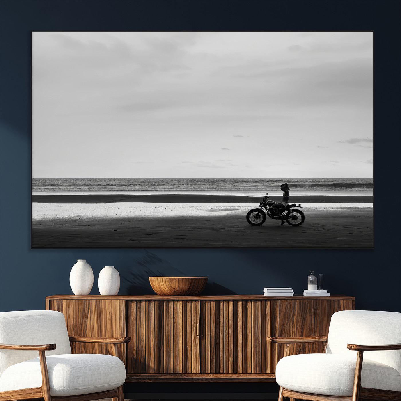 A motorcyclist on a vast beach, gazing at the ocean, capturing a moody and tranquil coastal adventure in black and white.
