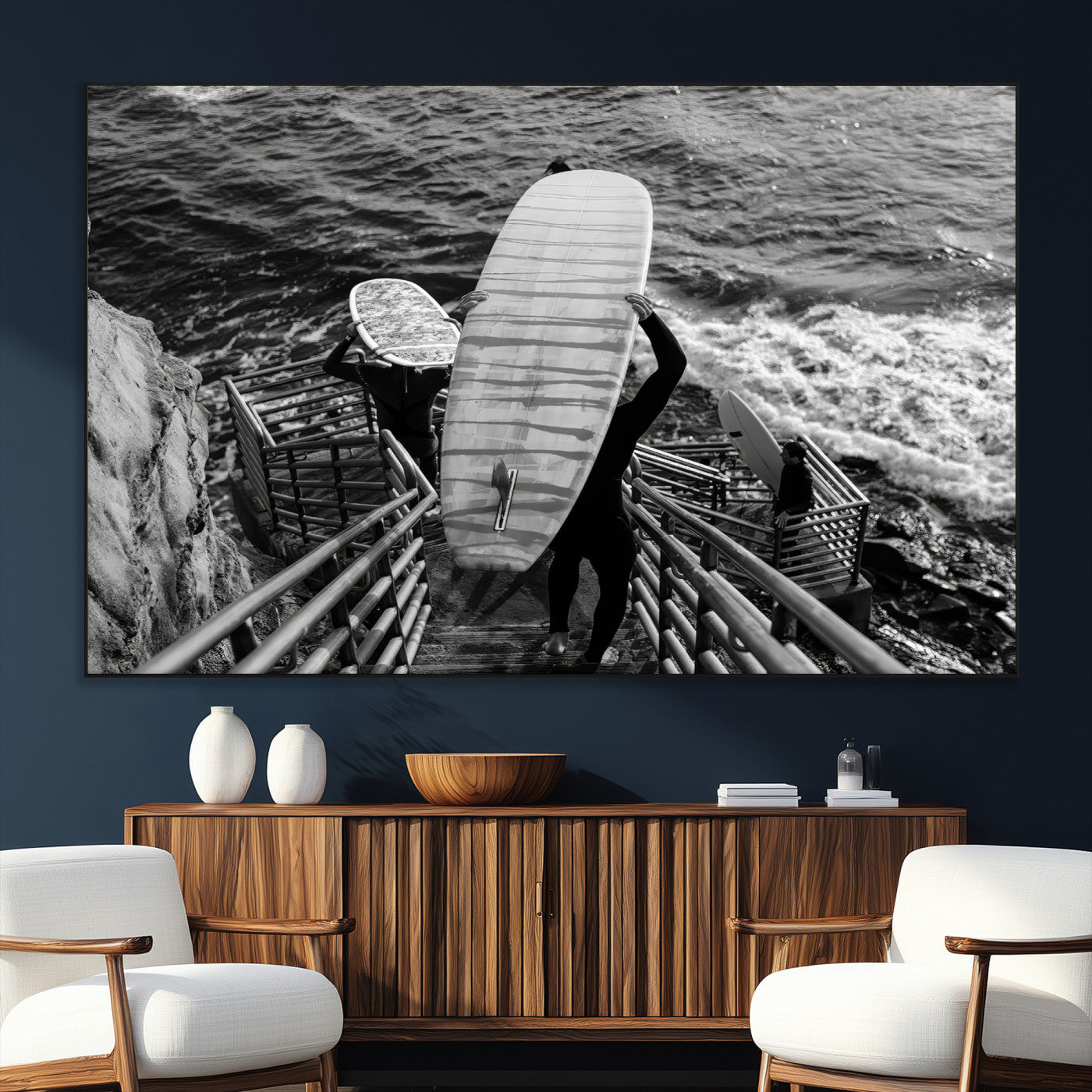 Black and white photo of surfers carrying boards down a rugged cliffside stairway, capturing a bold and adventurous coastal scene.
