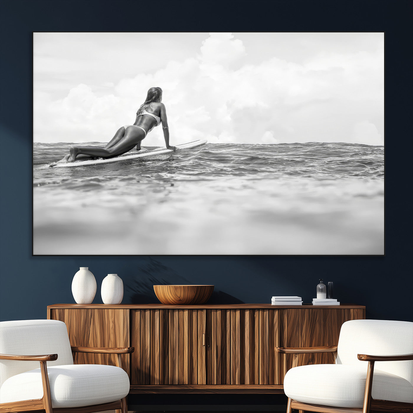A black and white ocean scene featuring a surfer girl waiting on her board, gazing at the horizon, capturing a tranquil and adventurous coastal moment.
