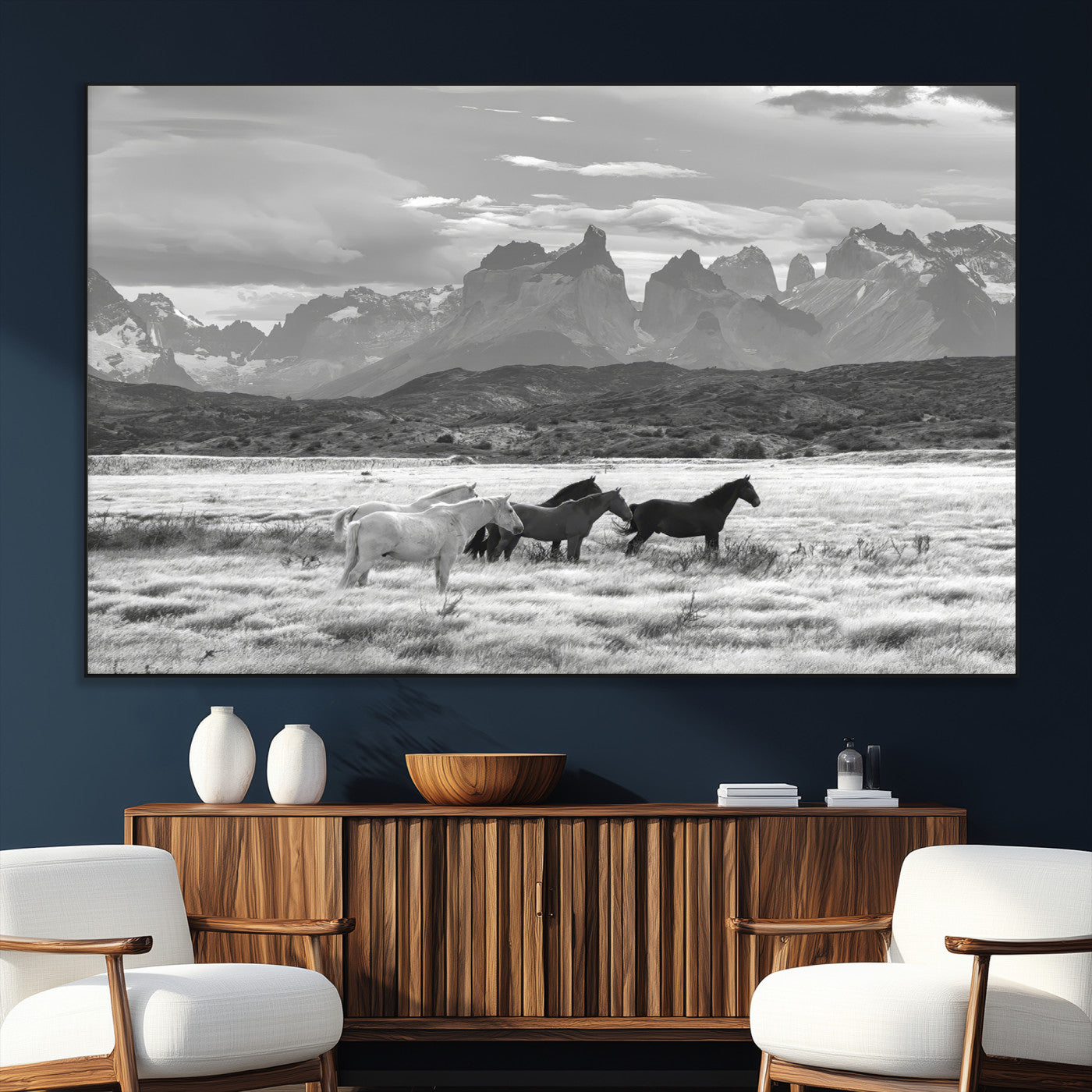 A black and white landscape of wild horses grazing in a vast grassland with towering mountains in the background, creating a moody and rustic western aesthetic.