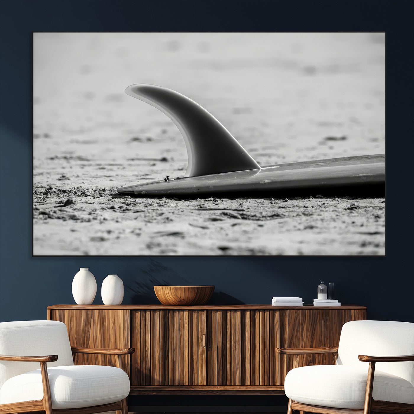 A black and white close-up of a surfboard fin resting on the sandy shore, highlighting minimalist beach aesthetics and classic surf culture.