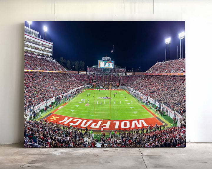 A NC State Wolfpack Football Team print of Carter-Finley Stadium at night features WOLFPACK illuminated brightly in the end zone grass.