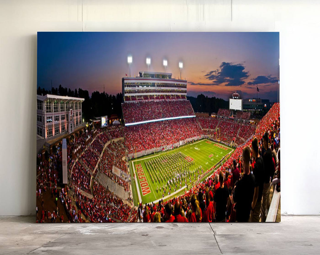 A print of a bustling Carter-Finley Stadium at dusk, featuring fans and a band, captures the essence of NC State Wolfpack football.