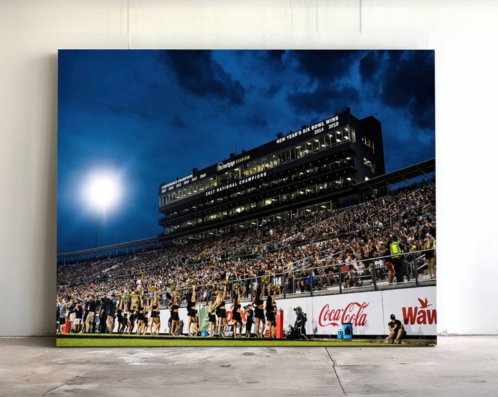 A gallery-quality canvas print depicting a stadium packed with fans under a night sky, highlighting the UCF Knights Football Team.