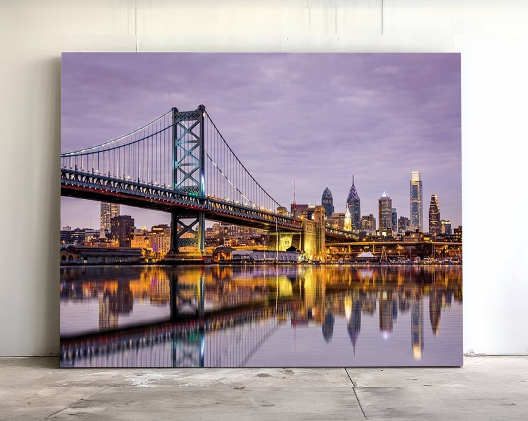 An Extra Large Wall Art Philadelphia Canvas Print, featuring a gallery-quality finish, captures the lit-up Ben Franklin Bridge and city buildings perfectly reflected on the water at sunset.