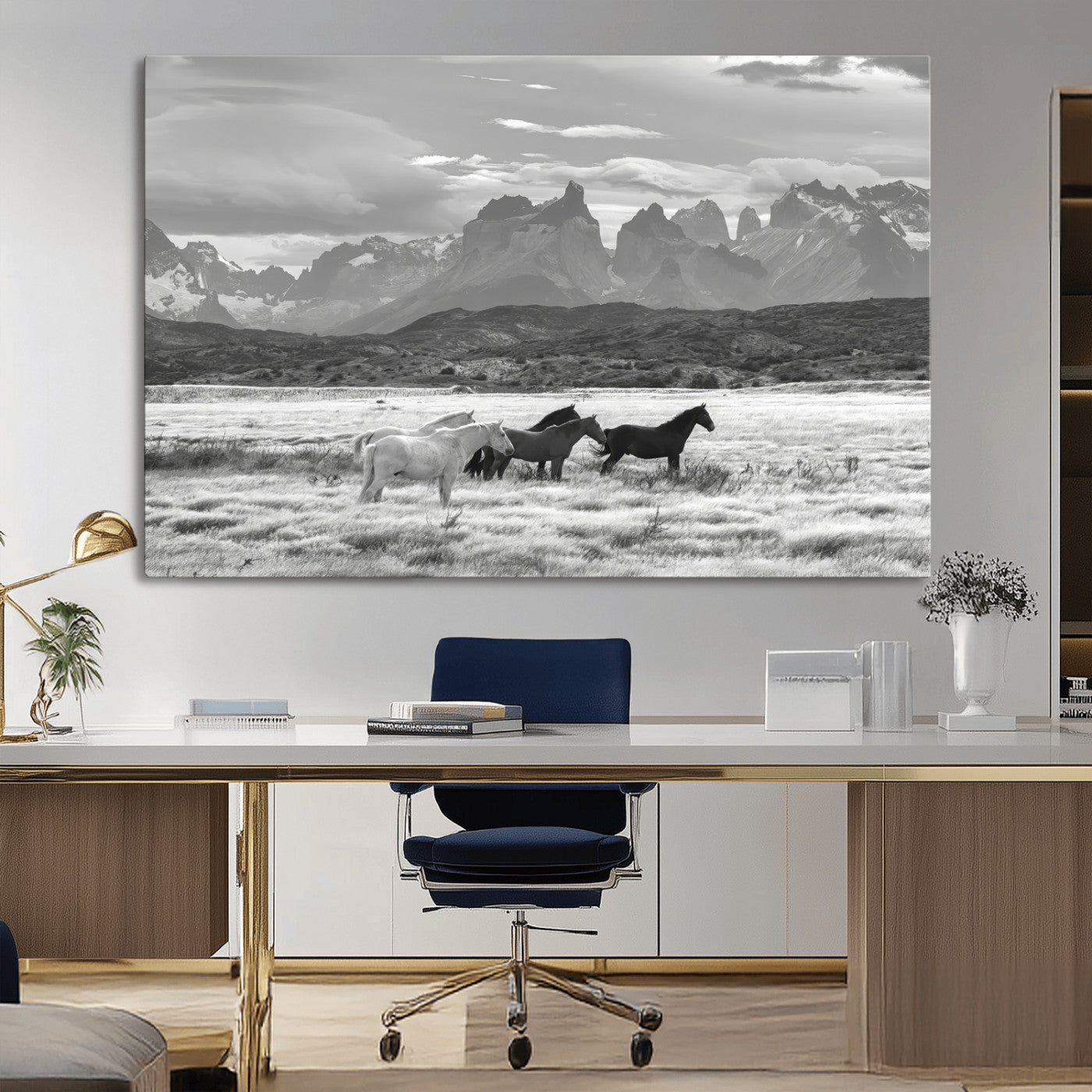 A black and white landscape of wild horses grazing in a vast grassland with towering mountains in the background, creating a moody and rustic western aesthetic.