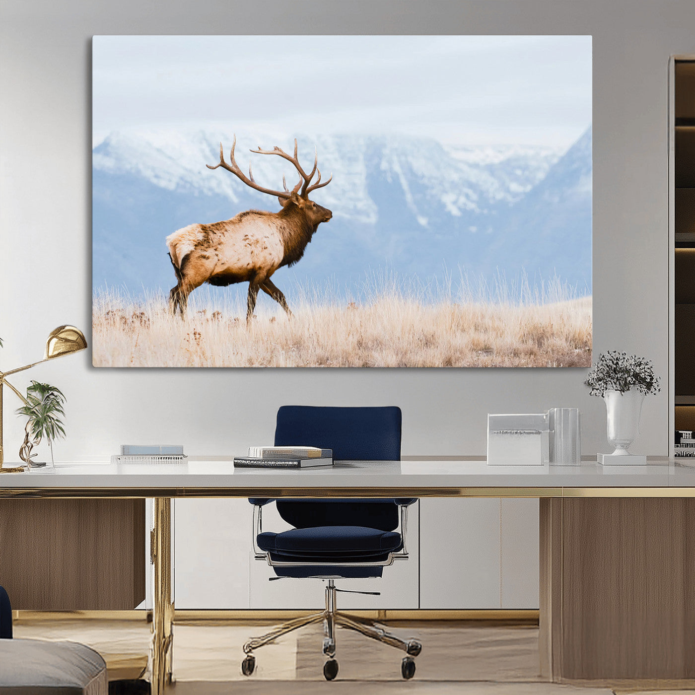 An elk walking on snowy grassland with majestic mountains in the background, ideal for rustic lodge or cabin wall decor.