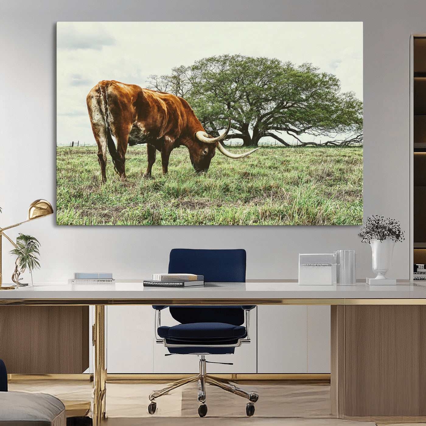 A Texas Longhorn grazing in a green pasture with a large tree in the background, evoking a rustic Western and farmhouse aesthetic.