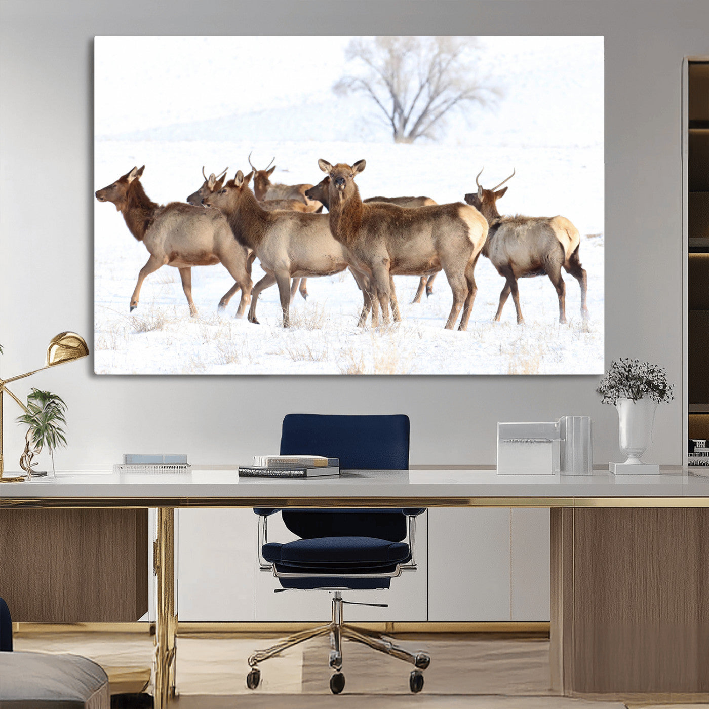 A herd of elk standing on snow-covered ground with a bare tree in the background, showcasing natural wildlife in a winter landscape.