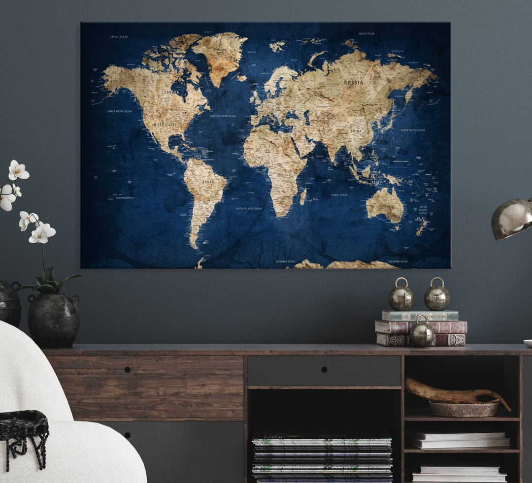 A large framed world map canvas print features beige landmasses set against a grunge-stained deep blue ocean background, creating an intriguing piece of wall art.