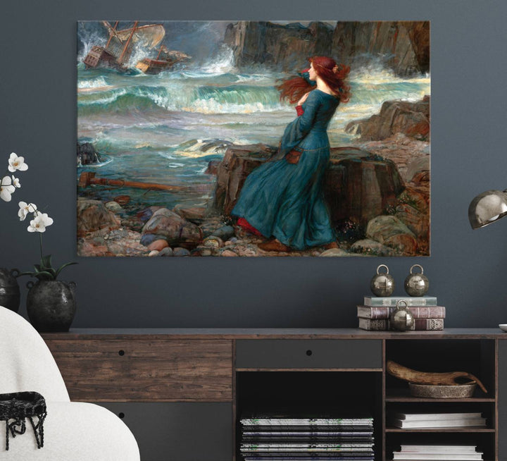 The Miranda by the Shore Wall Art Canvas Print depicts a woman in a blue dress standing by the sea, watching a shipwreck.