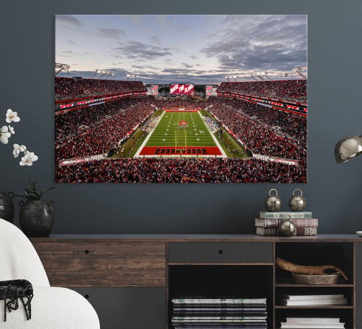 The wall art captures a stunning scene of Raymond James Stadium bathed in the warm hues of sunset. The sky, filled with clouds, provides a dramatic contrast to the vibrant lighting on the field, encapsulating the dynamic energy of a football game.