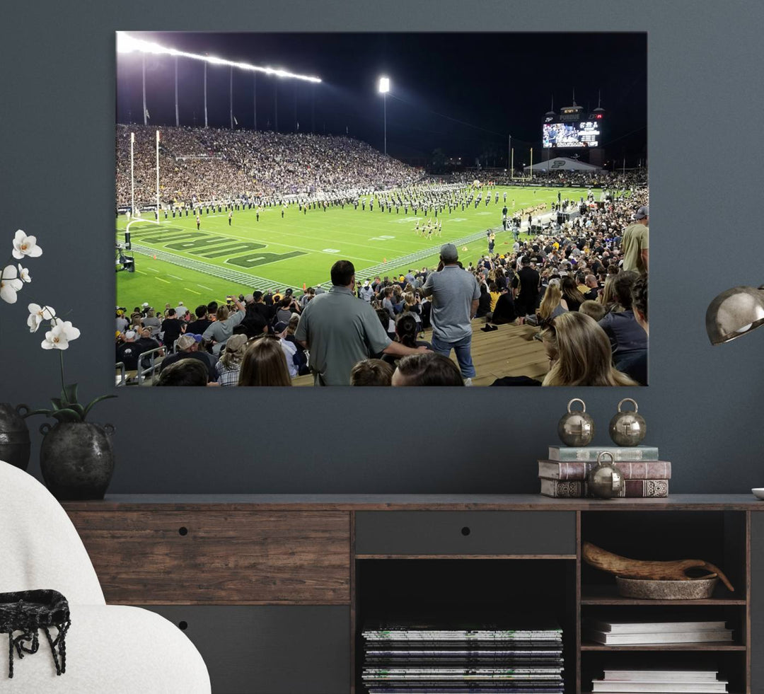 A painting depicting the Purdue Boilermakers football game at Ross-Ade Stadium is illuminated under gallery-quality lights.