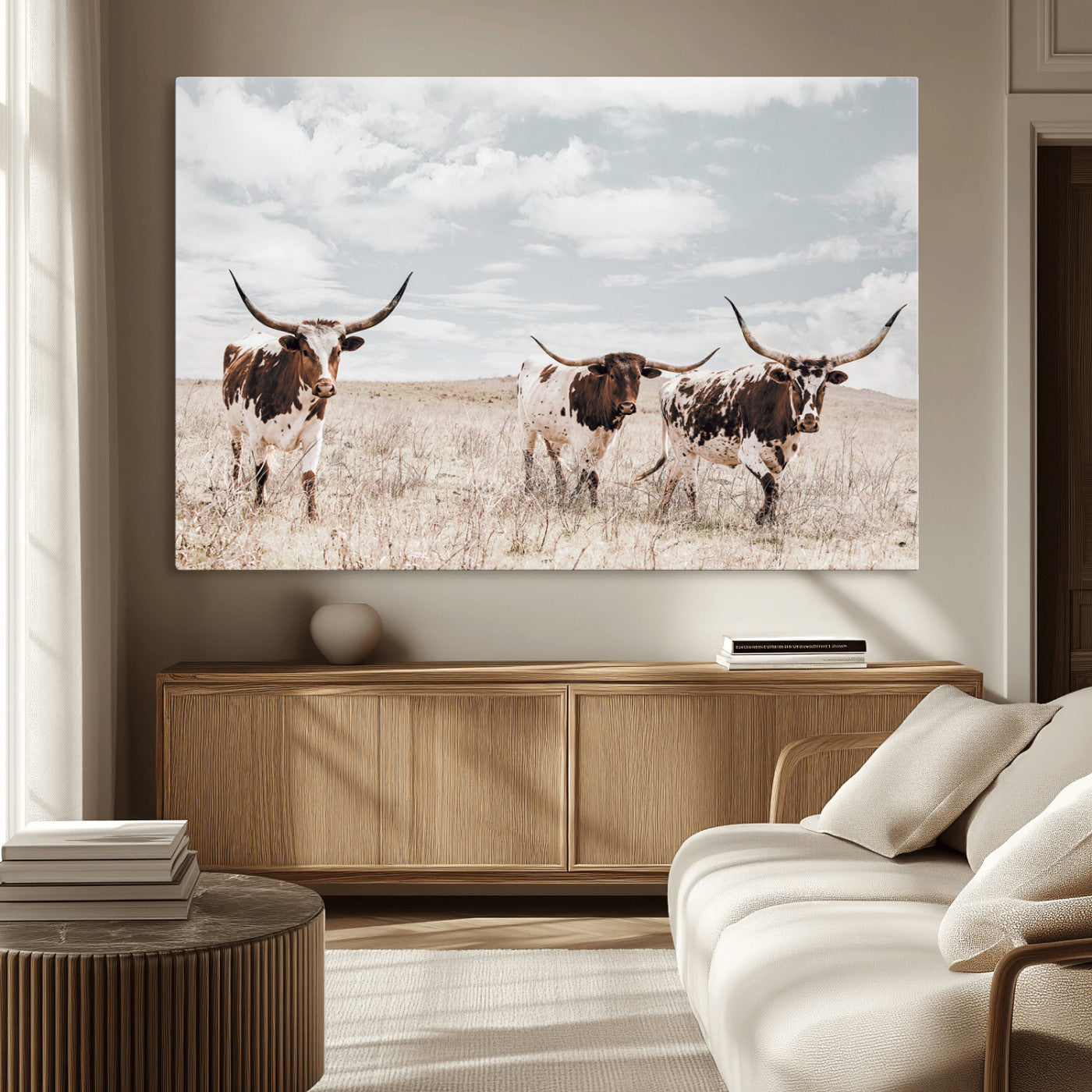 Three Texas Longhorn cattle walking through a dry grassy field under a partly cloudy sky.