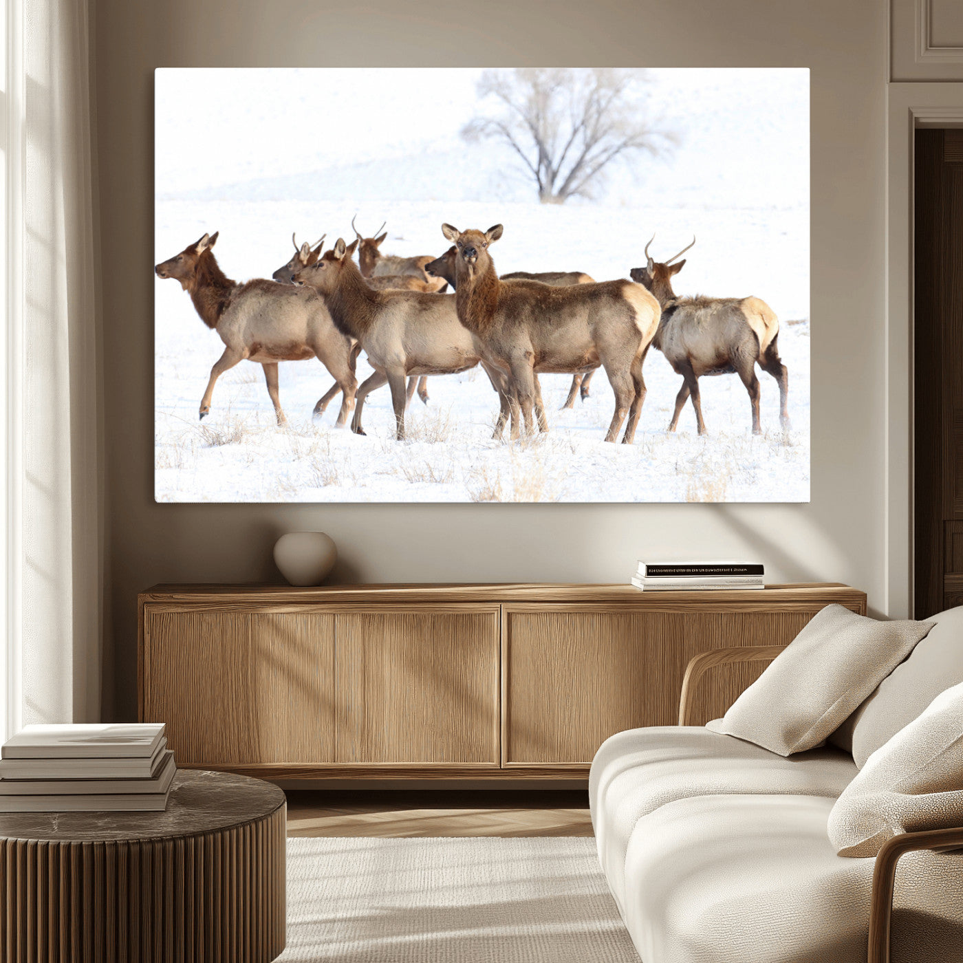 A herd of elk standing on snow-covered ground with a bare tree in the background, showcasing natural wildlife in a winter landscape.