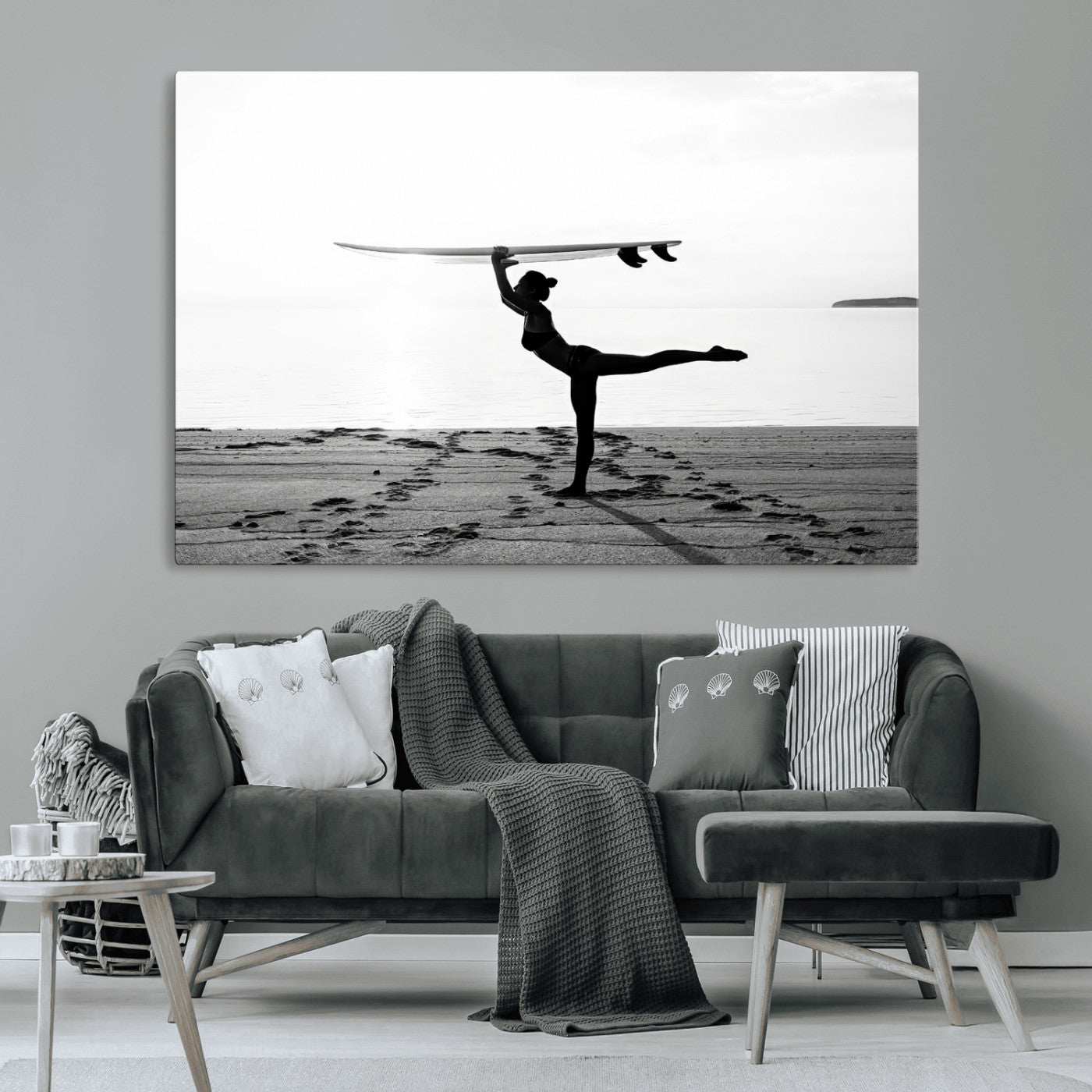 A woman balances a surfboard on her head while striking a yoga pose on the beach, silhouetted against a calm ocean horizon.