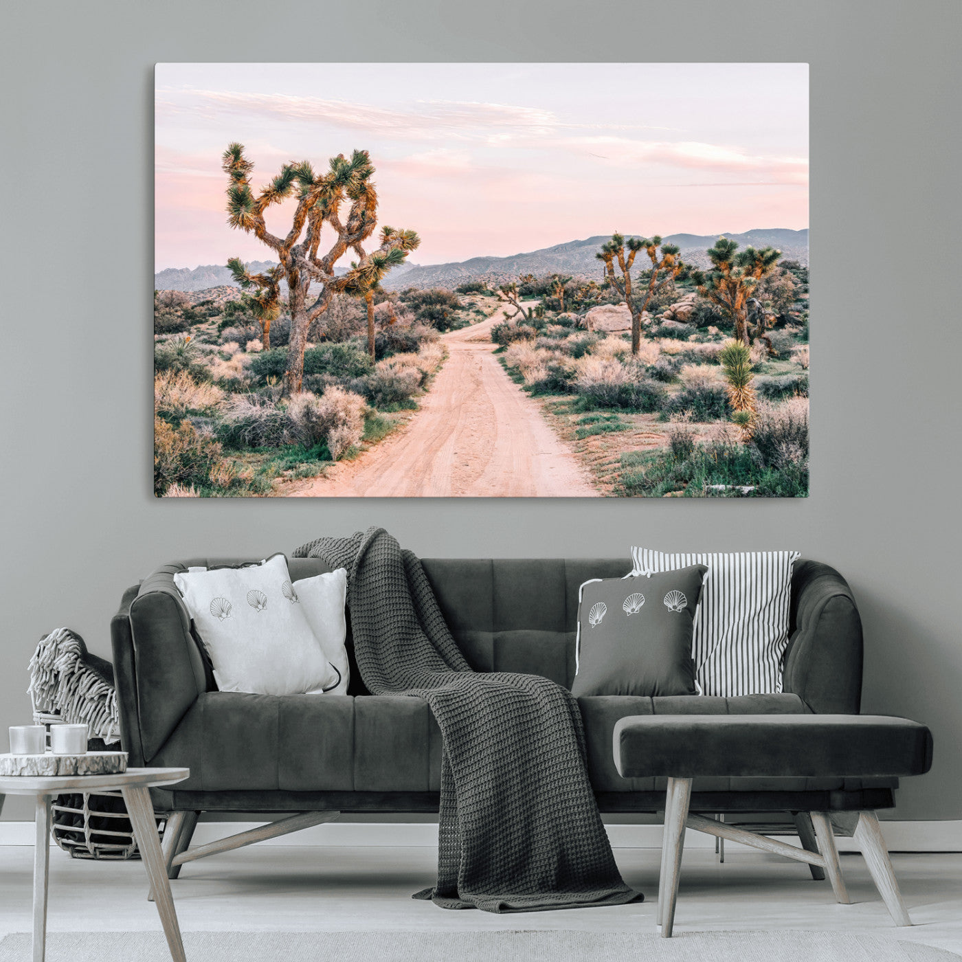A dusty road winding through Joshua Tree National Park, framed by iconic twisted trees and warm desert tones under a soft pastel sky.