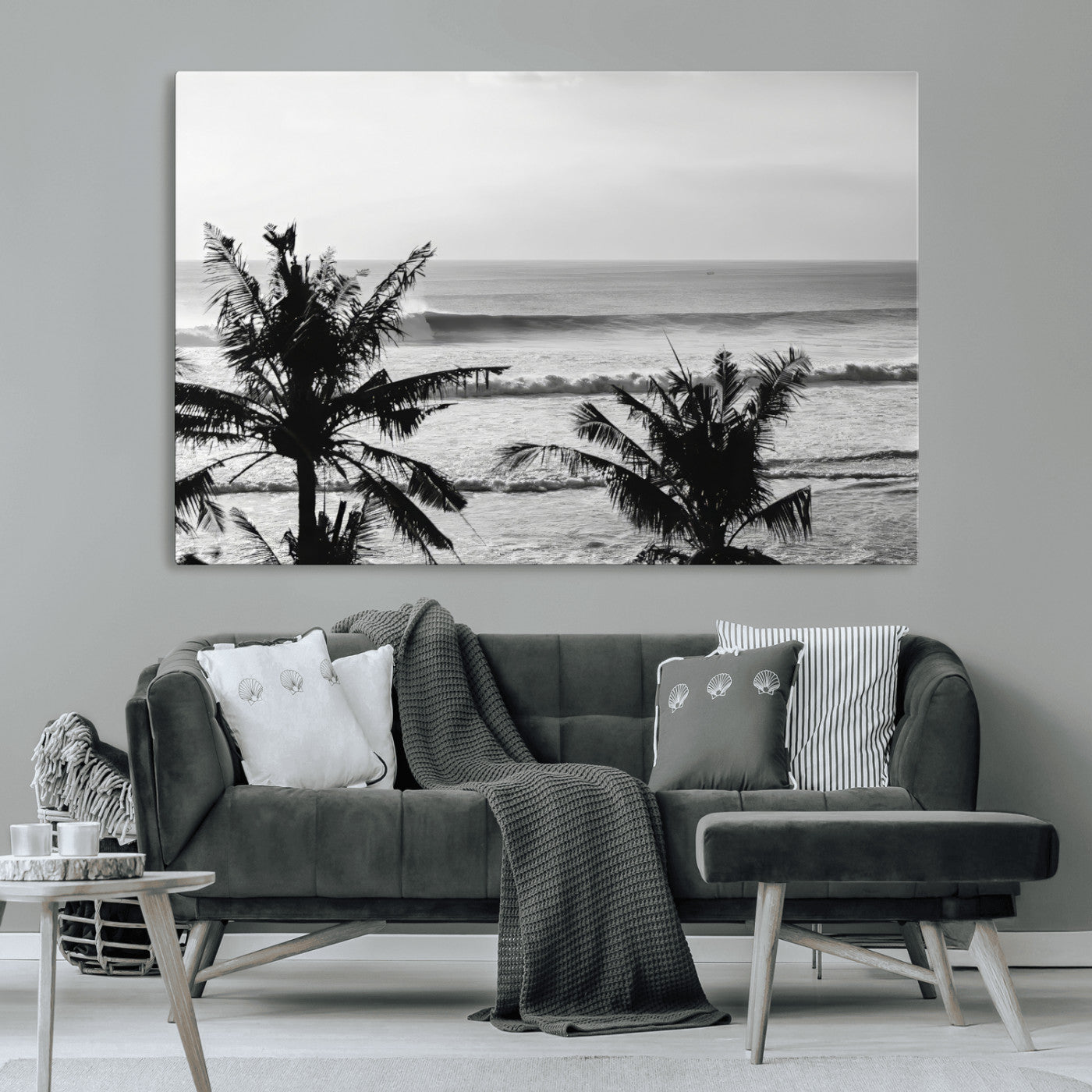Black and white view of ocean waves crashing on a tropical coastline, framed by silhouetted palm trees under a vast, open sky.