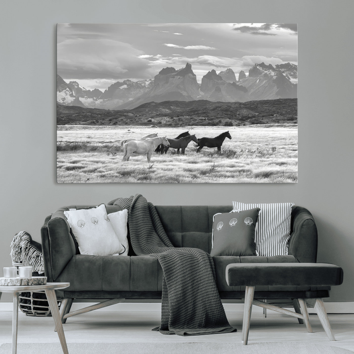 A black and white landscape of wild horses grazing in a vast grassland with towering mountains in the background, creating a moody and rustic western aesthetic.