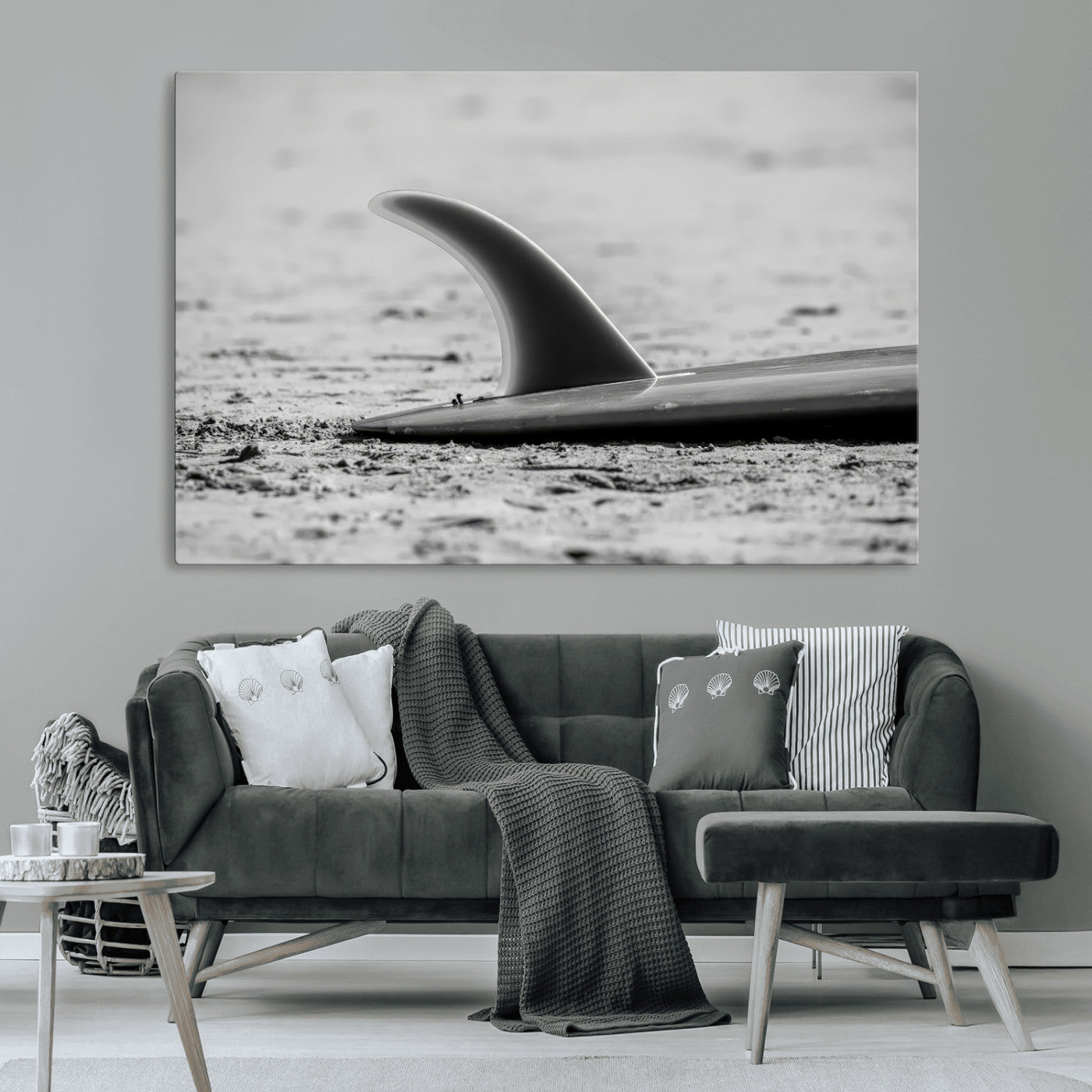 A black and white close-up of a surfboard fin resting on the sandy shore, highlighting minimalist beach aesthetics and classic surf culture.
