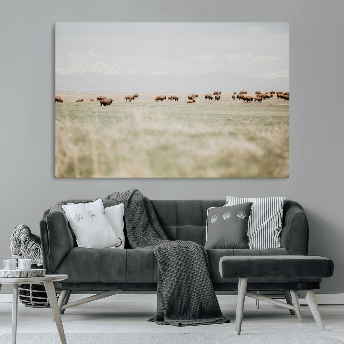A herd of bison grazing in an open prairie with distant mountains under a soft sky, creating a serene and rustic Western landscape.