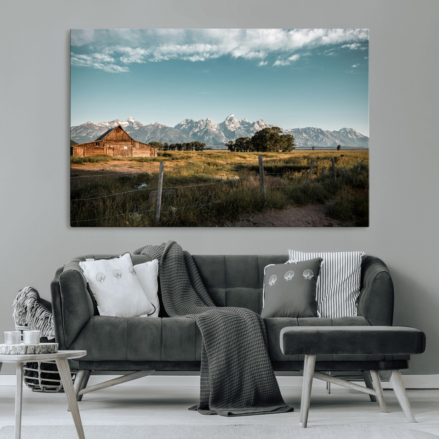 A rustic farmhouse with a wooden barn set against majestic mountain peaks under a soft blue sky, evoking peaceful countryside charm.