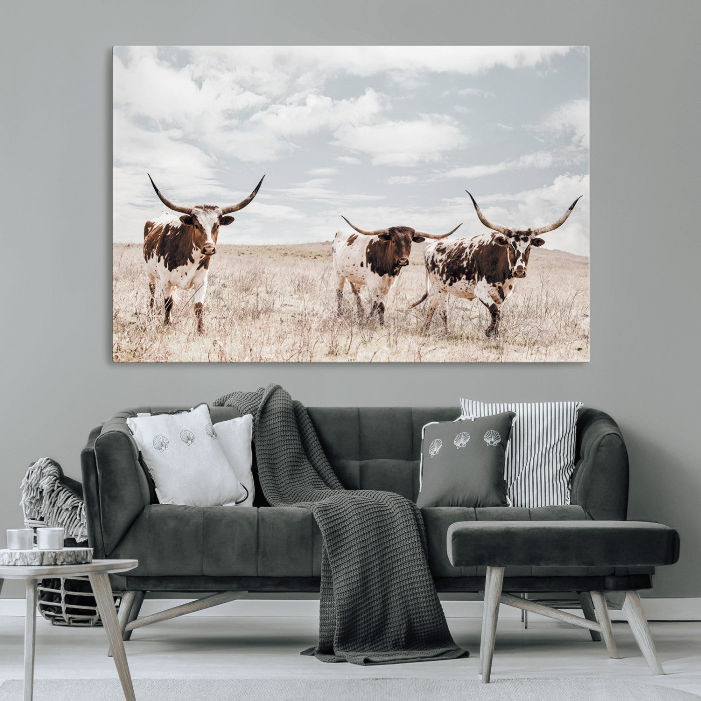 Three Texas Longhorn cattle walking through a dry grassy field under a partly cloudy sky.
