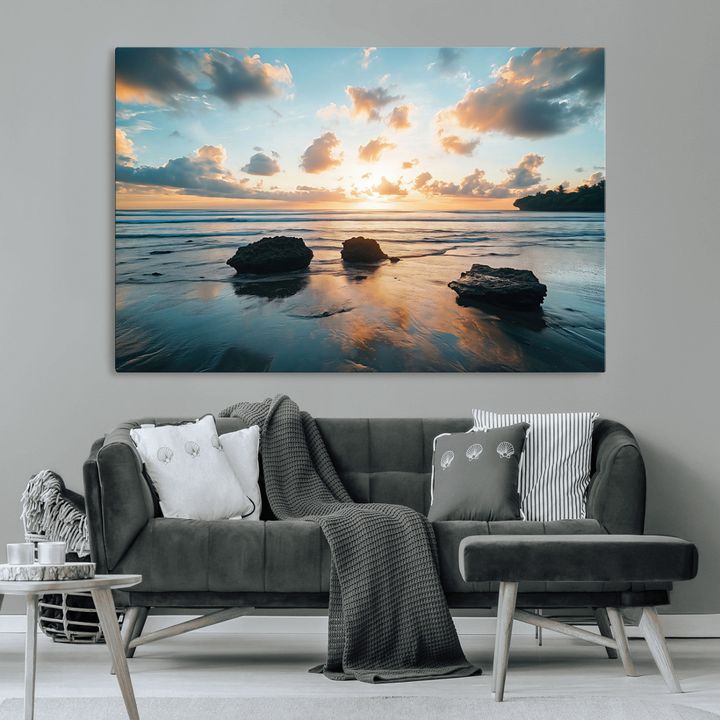 A serene beach at sunset with vibrant clouds, calm water, and rocks in the foreground reflecting the warm colors of the setting sun.