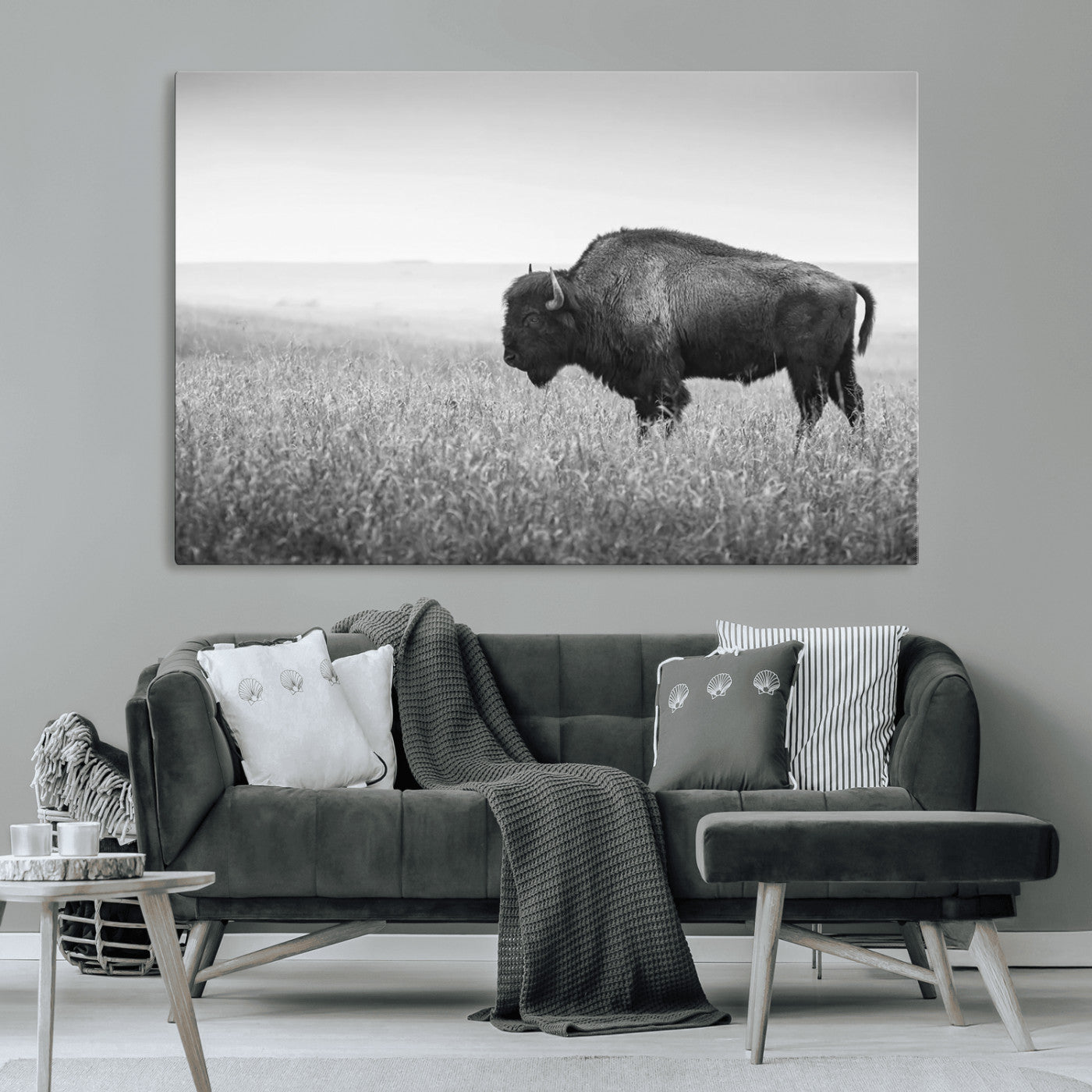 "Black and white image of a bison grazing in a vast field under an overcast sky."