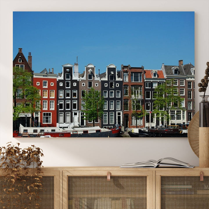 The Amsterdam City Wall Art Canvas Print showcases colorful traditional canal houses and boats set against a clear blue sky.