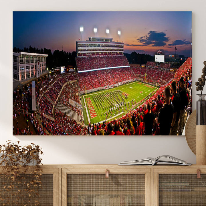 A print of a bustling Carter-Finley Stadium at dusk, featuring fans and a band, captures the essence of NC State Wolfpack football.