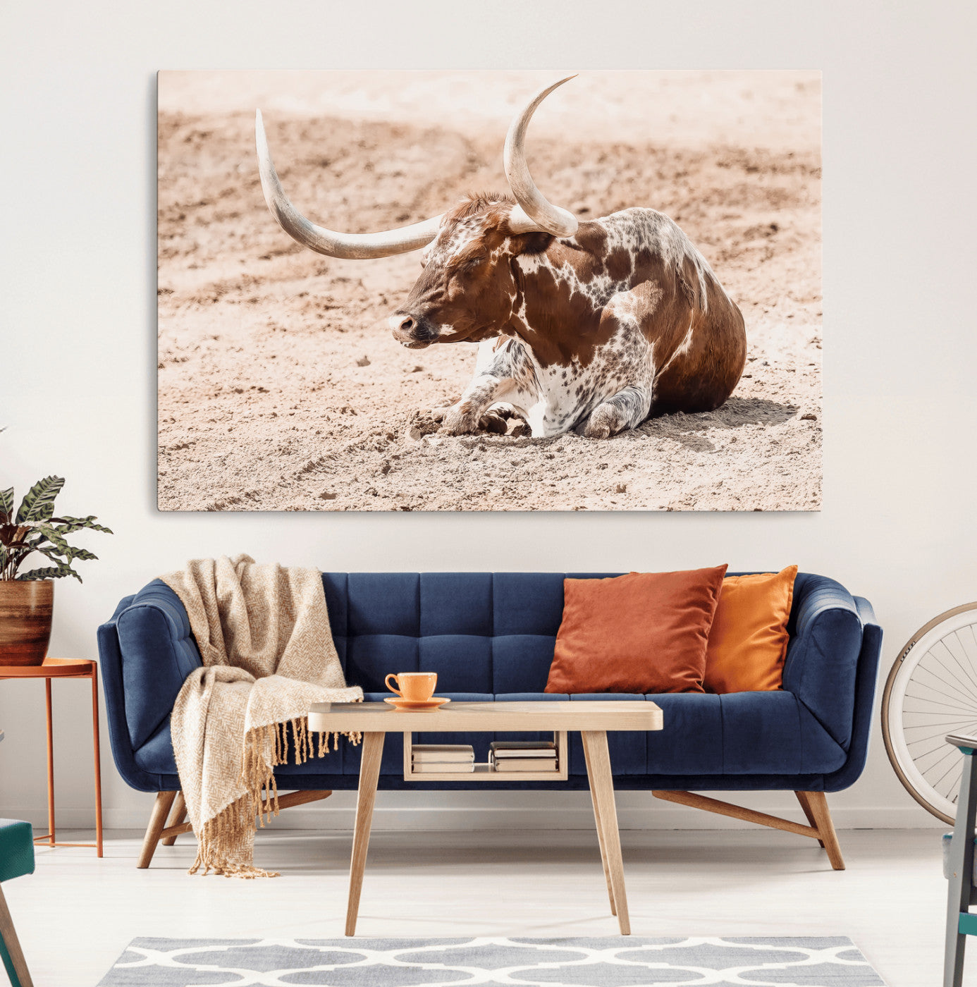 Texas Longhorn bull resting on dusty ground with warm tones, ideal for rustic western or farmhouse-themed wall decor.
