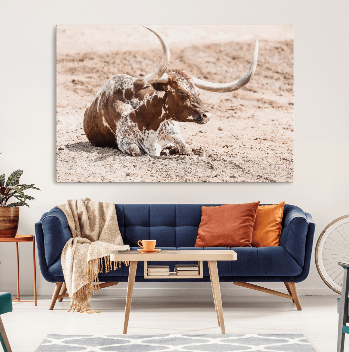 Texas Longhorn bull resting on dusty ground with warm tones, ideal for rustic western or farmhouse-themed wall decor.