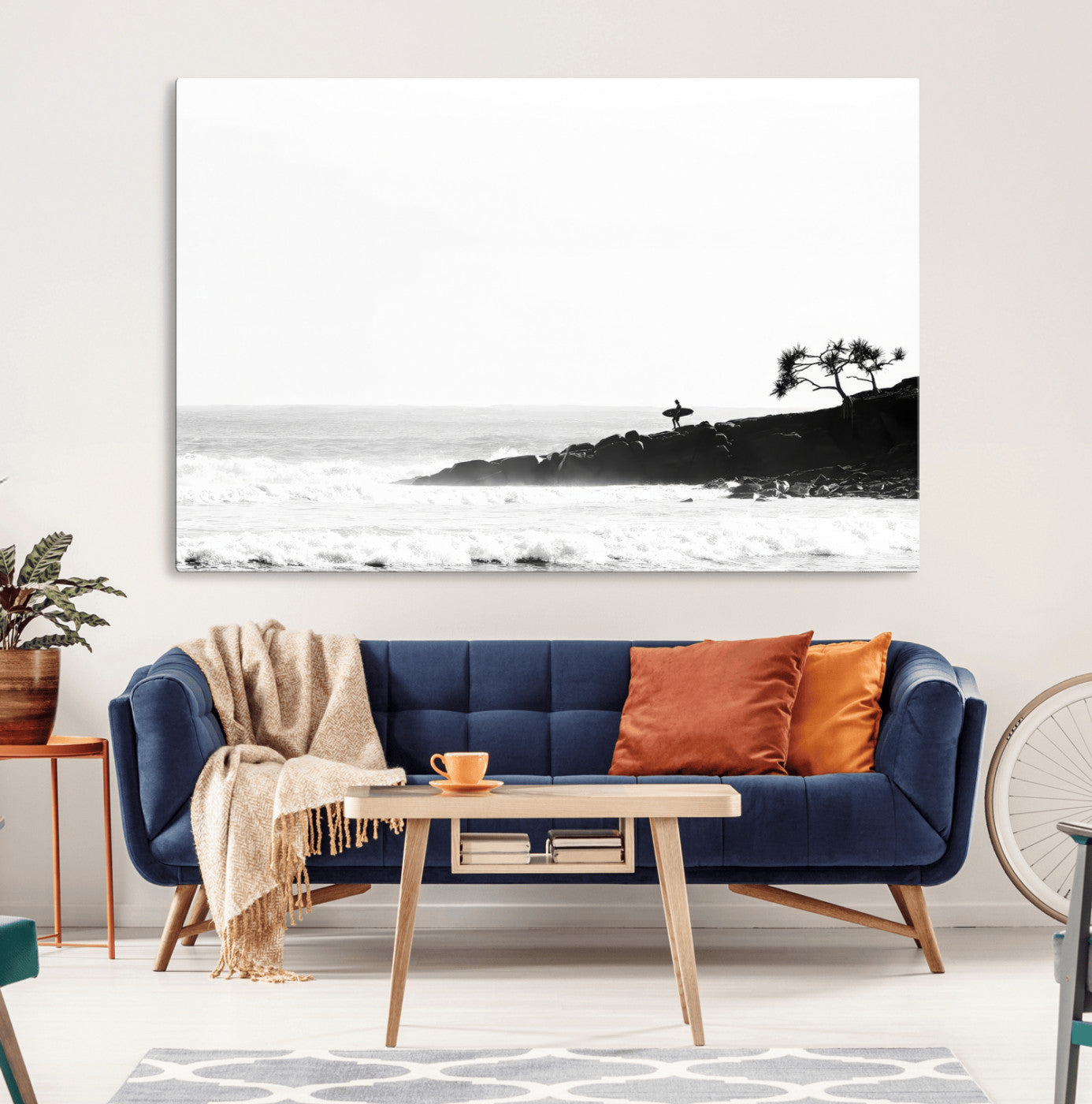 Black and white photo of a surfer standing on rocky cliffs, gazing at the waves, embodying the spirit of adventure and solitude.