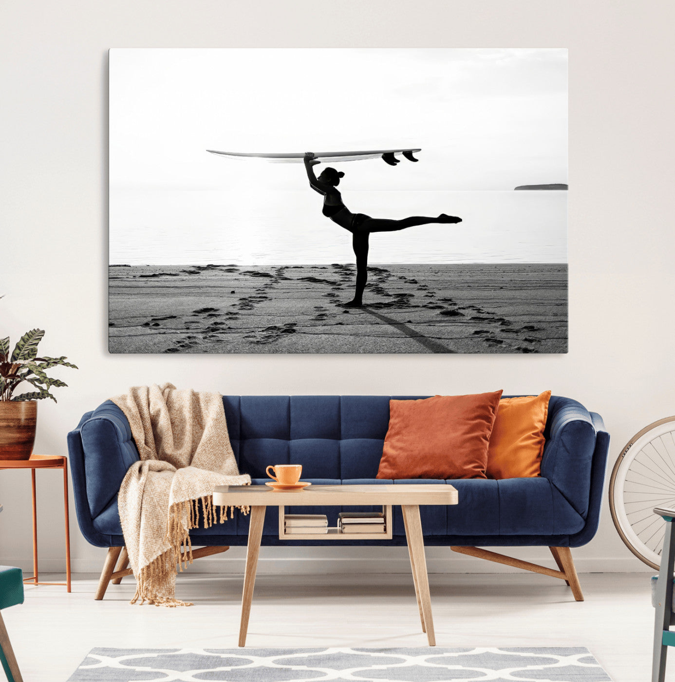 A woman balances a surfboard on her head while striking a yoga pose on the beach, silhouetted against a calm ocean horizon.