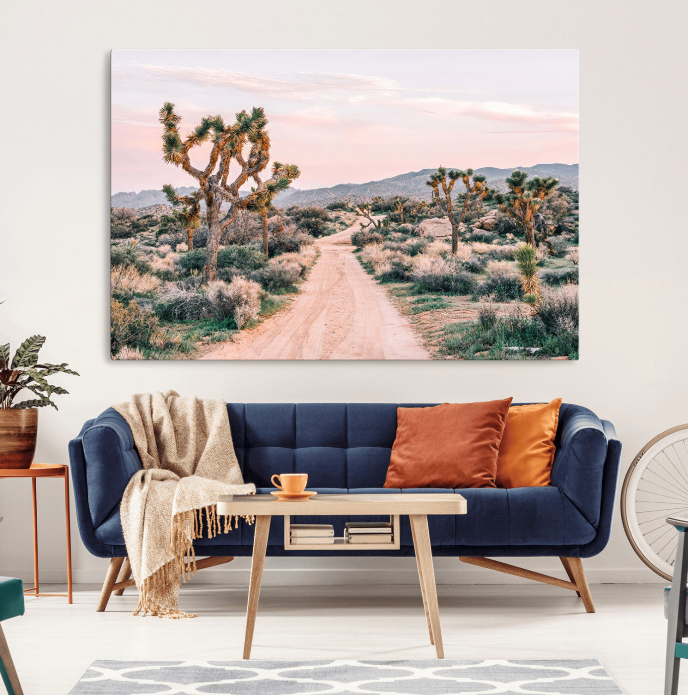 A dusty road winding through Joshua Tree National Park, framed by iconic twisted trees and warm desert tones under a soft pastel sky.