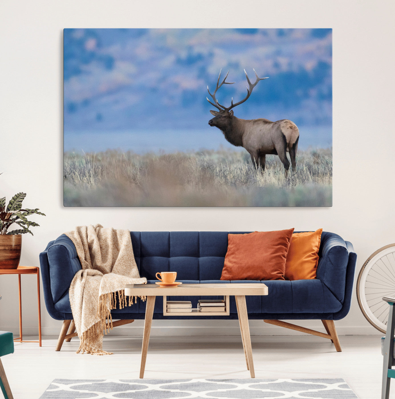 Elk with large antlers standing in open field, mountains blurred in background, perfect for rustic cabin or lodge-style decor.