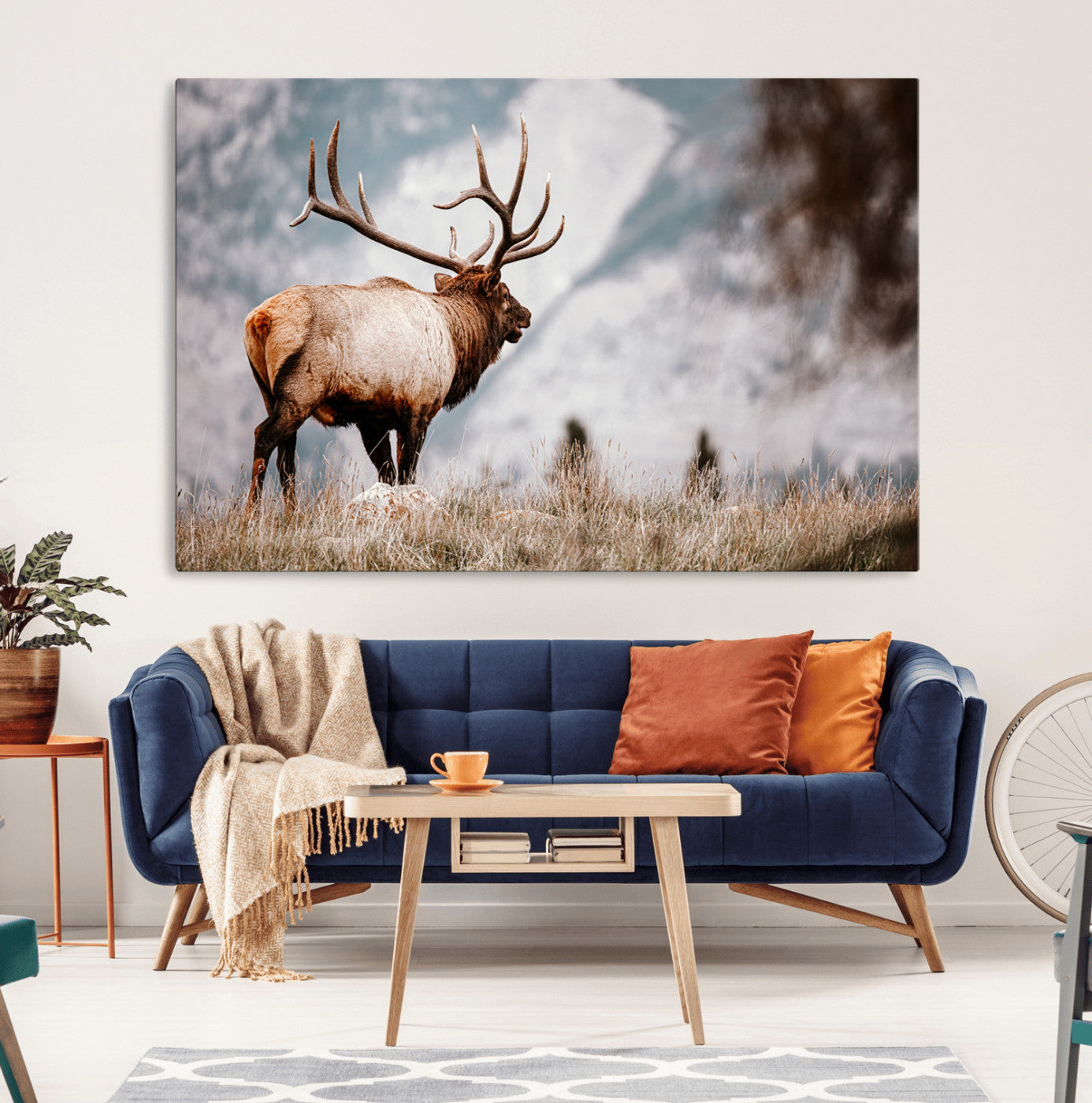 Majestic elk with large antlers standing in grass with snowy mountains in background, perfect for rustic cabin or lodge style decor.