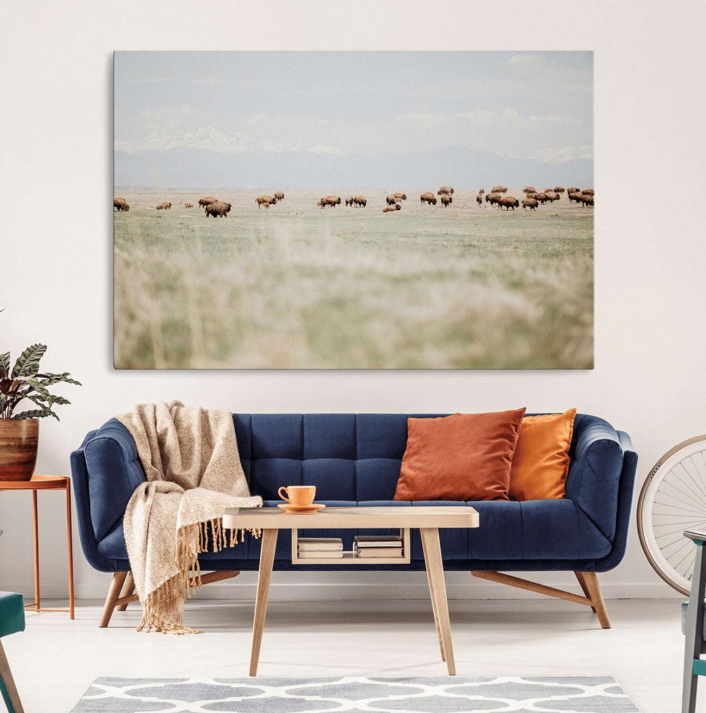 A herd of bison grazing in an open prairie with distant mountains under a soft sky, creating a serene and rustic Western landscape.