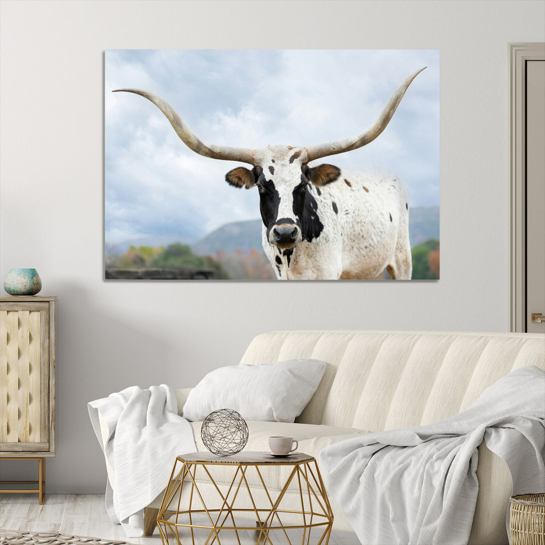 Close-up of a Texas Longhorn with curved horns, black and white markings, set against a cloudy sky and distant hills, perfect for rustic decor.